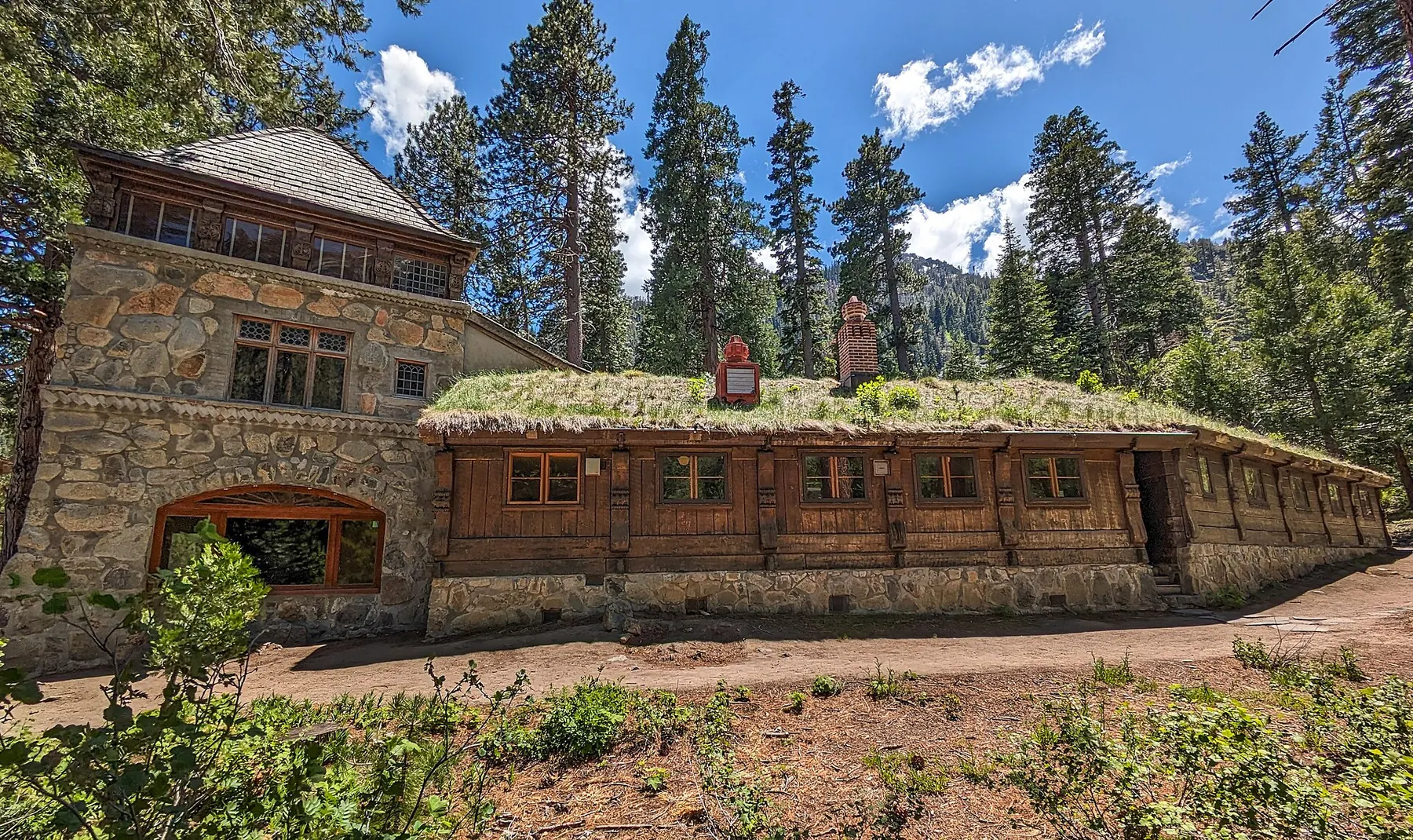 The sod-roofed timber and stone wing of Vikingsholm under tall pines and a blue sky